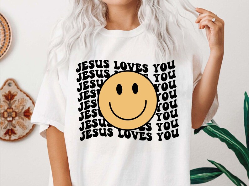 May include: White t-shirt with a black and yellow smiley face and the text "JESUS LOVES YOU" repeated in a retro font.