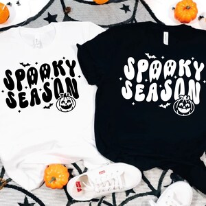 May include: Two t-shirts with the text "Spooky Season" in a retro font. The shirts are black and white and feature a pumpkin and bats.