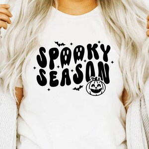 May include: White t-shirt with a black graphic that says "Spooky Season" in a retro font. The graphic also includes a pumpkin and bats.