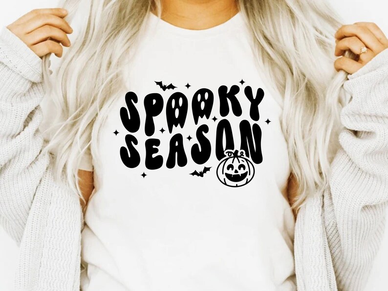 May include: White t-shirt with a black graphic that says "Spooky Season" in a retro font. The graphic also includes a pumpkin and bats.