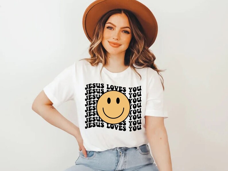 May include: White t-shirt with a yellow smiley face and the text "JESUS LOVES YOU" repeated in black.