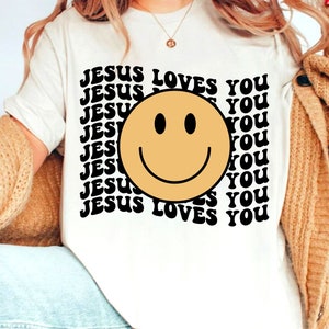 May include: White t-shirt with a black and yellow smiley face and the text "JESUS LOVES YOU" repeated in a retro font.