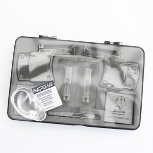 May include: A gray plastic ear piercing kit with a clear lid. The kit contains practice ears, piercing instruments, and skin cleansing pads. The text "Practice Ear" and "Studex" are visible on the packaging.