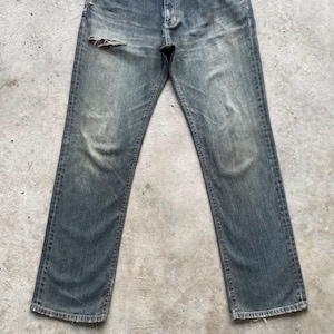 May include: Faded blue denim jeans with a distressed look. The jeans have a worn appearance with a tear on the upper left leg. The jeans have a classic five-pocket design and a straight leg cut.