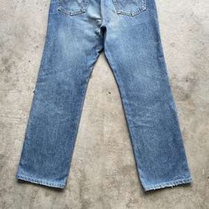 May include: Light blue denim jeans with a classic five-pocket design. The jeans have a faded wash and a straight leg cut. The back pockets are visible, and the jeans appear to be pre-worn.