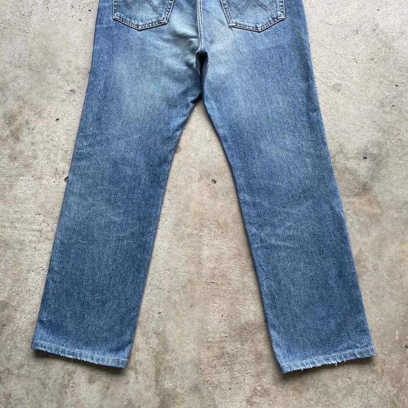 May include: Light blue denim jeans with a classic five-pocket design. The jeans have a faded wash and a straight leg cut. The back pockets are visible, and the jeans appear to be pre-worn.