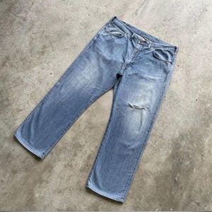K&ouml;nnte beinhalten: Hellblaue Jeans mit einem aufgerissenen Knie. Die Jeans haben ein klassisches F&uuml;nf-Taschen-Design und eine gerade Beinpassform. Der Denim hat ein verwaschenes Aussehen.