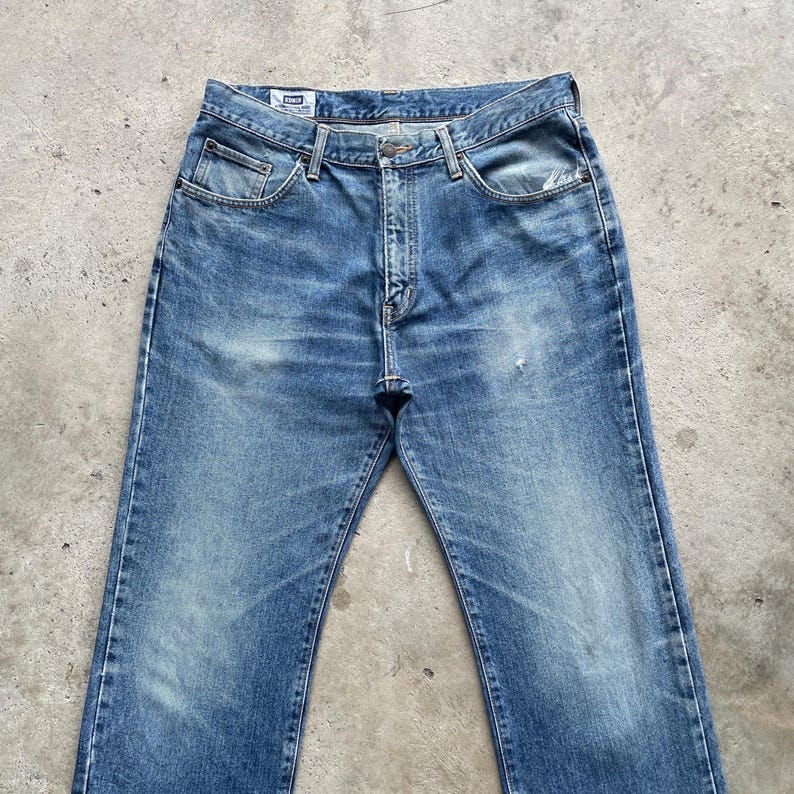 May include: Faded blue denim jeans with a classic five-pocket design. The jeans show signs of wear and fading, with a button and zipper closure. The jeans have a straight leg cut and are suitable for casual wear.