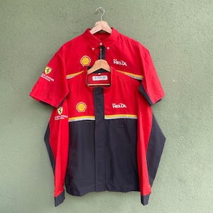 May include: A red and black racing jacket and short-sleeved shirt set. The jacket and shirt feature Shell and Helix logos, with yellow and white accents. The shirt has a button-down collar. The jacket has a zipper closure and a small pocket.