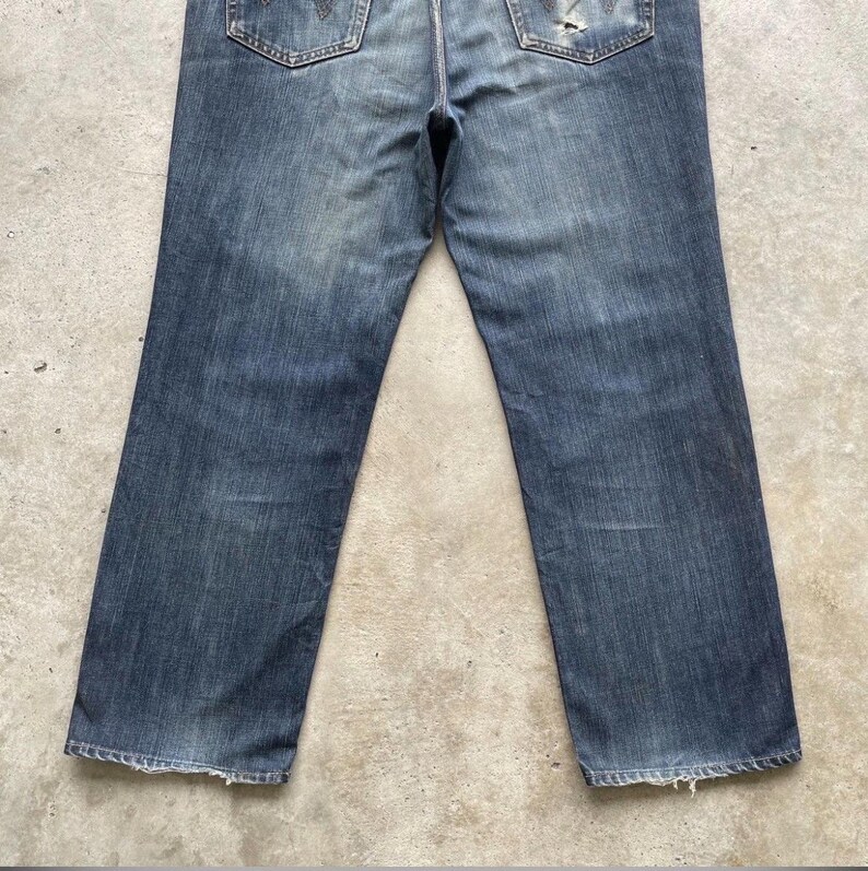 K&ouml;nnte beinhalten: Verblasste blaue Jeans mit klassischem F&uuml;nf-Taschen-Design. Die Jeans weisen Gebrauchsspuren auf, mit abgenutzten Details und einem eingetragenen Aussehen. Die Ges&auml;&szlig;taschen haben eine dekorative Naht.