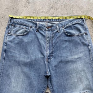 K&ouml;nnte beinhalten: Hellblaue Jeans mit einem gelben Ma&szlig;band &uuml;ber der Taille. Die Jeans haben ein klassisches F&uuml;nf-Taschen-Design und einen Knopf- und Rei&szlig;verschluss. Die Taille misst ca. 56 cm.
