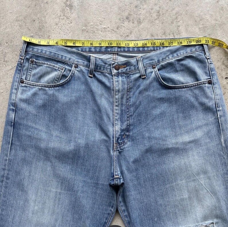 K&ouml;nnte beinhalten: Hellblaue Jeans mit einem gelben Ma&szlig;band &uuml;ber der Taille. Die Jeans haben ein klassisches F&uuml;nf-Taschen-Design und einen Knopf- und Rei&szlig;verschluss. Die Taille misst ca. 56 cm.