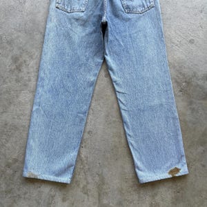 May include: Light blue denim jeans with a faded wash and a straight leg fit. The jeans have two back pockets and show signs of wear, including discoloration near the hem. The jeans are a classic style.