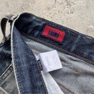 K&ouml;nnte beinhalten: Nahaufnahme einer dunkelblauen Edwin 503 Regular Jeans. Die Jeans hat ein rotes Etikett mit wei&szlig;em Text "Edwin 503 Regular". Ein wei&szlig;es Etikett zeigt die Gr&ouml;&szlig;e 38x33 und weitere Informationen. Die Jeans ist aus Denim.