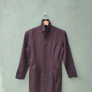 May include: A dark brown, long-sleeved coat with a high collar and a row of buttons down the front. The coat has two pockets and is hanging on a wooden hanger.