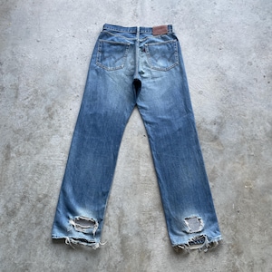 Pu&ograve; includere: Jeans di denim blu sbiadito con dettagli usurati, tra cui ginocchia strappate e un aspetto vissuto. I jeans presentano il classico stile a cinque tasche, una chiusura con bottone e cerniera e una toppa in pelle marrone sul retro.