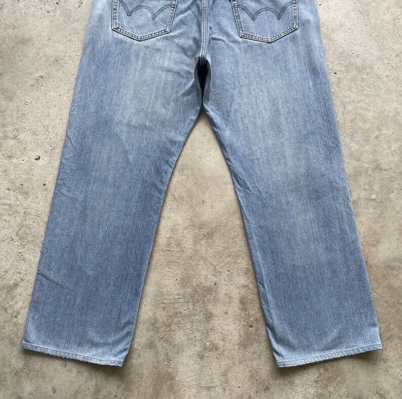 K&ouml;nnte beinhalten: Hellblaue Jeans mit klassischem F&uuml;nf-Taschen-Design. Die Jeans haben eine verwaschene Optik und einen geraden Beinverlauf. Die Ges&auml;&szlig;taschen haben ein markantes Nahtmuster. Die Jeans liegen flach auf einer neutralen Oberfl&auml;che.
