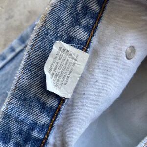 May include: Close-up of blue denim jeans with a white care label. The label includes washing instructions: machine wash warm, wash darks separately, only non-chlorine bleach when needed, tumble medium, warm iron when necessary.