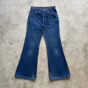 May include: Dark blue denim jeans with a flared leg design. The jeans have a button and zipper closure, front and back pockets, and belt loops. The denim has a faded appearance in areas.