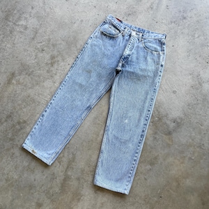 May include: Light blue acid wash denim jeans. The jeans have a classic five-pocket design with a button and zipper closure. The denim has a faded, worn appearance, with some light discoloration. The jeans are laid flat on a concrete surface.
