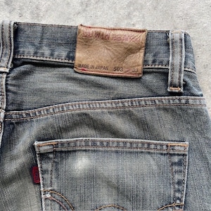 Puede incluir: Primer plano de vaqueros de mezclilla azul descoloridos. El bolsillo trasero tiene una etiqueta roja. Un parche de cuero marr&oacute;n en la cintura dice "EDWIN" y "MADE IN JAPAN 503 33". Los vaqueros tienen costuras visibles y un aspecto desgastado.
