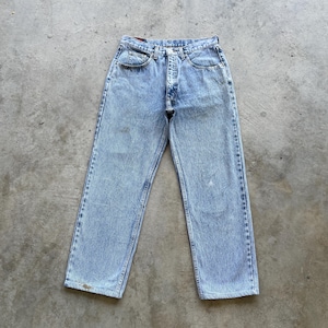 May include: Light blue denim jeans with a classic five-pocket design. The jeans have a straight leg cut and a button and zipper closure. The denim has a faded wash and some minor wear marks, giving them a vintage look.
