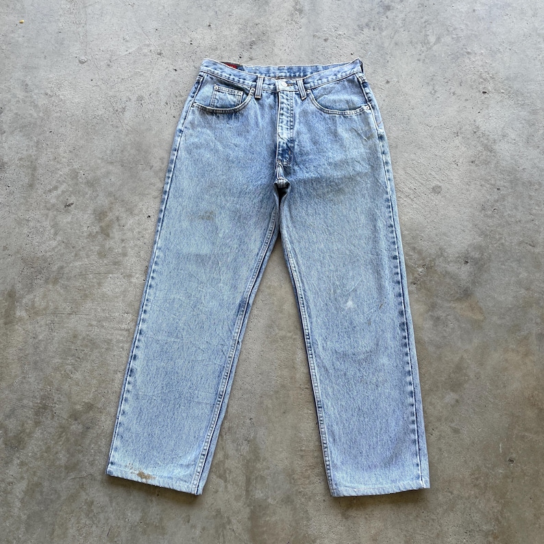 May include: Light blue denim jeans with a classic five-pocket design. The jeans have a straight leg cut and a button and zipper closure. The denim has a faded wash and some minor wear marks, giving them a vintage look.