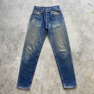 May include: Faded blue denim jeans with a classic five-pocket design. The jeans show signs of wear with lighter patches on the thighs and knees, giving them a vintage look. The jeans are laid flat on a concrete surface.