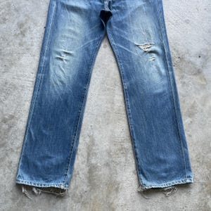 Pu&ograve; includere: Jeans in denim blu sbiadito con dettagli strappati. I jeans hanno un classico design a cinque tasche, una chiusura con bottone e cerniera e una vestibilit&agrave; dritta. Il denim mostra segni di usura, con alcune aree sbiadite e strappate.