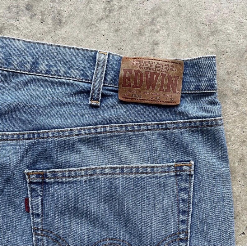 K&ouml;nnte beinhalten: Nahaufnahme einer hellblauen Jeans mit einem braunen Lederaufn&auml;her mit der Aufschrift "EDWIN". Die Jeans hat ein klassisches F&uuml;nf-Taschen-Design mit einem roten Etikett auf der Ges&auml;&szlig;tasche. Gr&ouml;&szlig;e W42 L33.