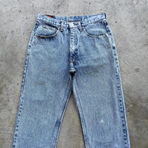 May include: Light blue denim jeans with a classic five-pocket design. The jeans have a faded wash and a straight leg cut. The jeans are made of a durable denim material and feature a button and zipper closure.
