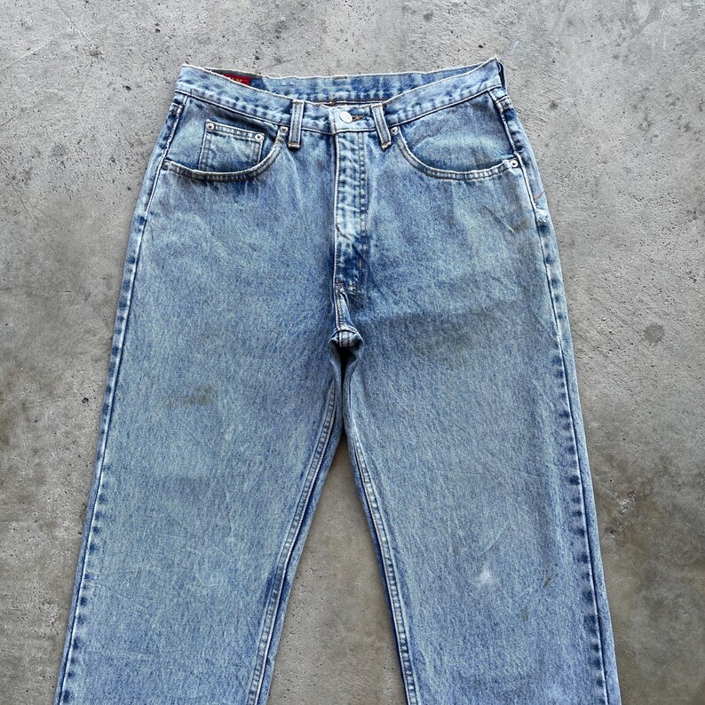 May include: Light blue denim jeans with a classic five-pocket design. The jeans have a faded wash and a straight leg cut. The jeans are made of a durable denim material and feature a button and zipper closure.
