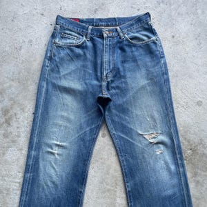 Pu&ograve; includere: Jeans in denim blu sbiadito con dettagli strappati, tra cui strappi e segni di usura. I jeans hanno un classico design a cinque tasche, una chiusura con bottone e cerniera e una vestibilit&agrave; dritta. Il denim ha un aspetto vintage e usurato.