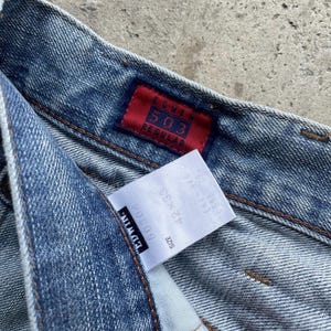 K&ouml;nnte beinhalten: Nahaufnahme einer hellblauen Jeans mit einem roten Edwin 503 Regular-Etikett. Ein wei&szlig;es Etikett zeigt die Gr&ouml;&szlig;e 42x33. Die Jeans hat ein klassisches F&uuml;nf-Taschen-Design und ein verwaschenes Aussehen.