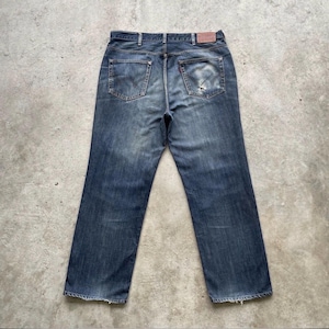K&ouml;nnte beinhalten: Verblasste blaue Jeans mit klassischem F&uuml;nf-Taschen-Design. Die Jeans haben ein abgenutztes Aussehen mit abgenutzten Details, einschlie&szlig;lich eines kleinen Risses an der Ges&auml;&szlig;tasche. Ein brauner Lederaufn&auml;her ist am Bund sichtbar.
