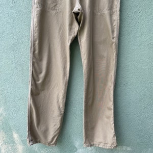 May include: Khaki-coloured trousers with a straight leg design. The trousers have visible stitching along the seams and pockets. The fabric appears to be a lightweight material, suitable for casual wear.