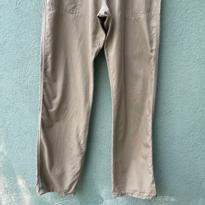 May include: Khaki-coloured trousers with a straight leg design. The trousers have visible stitching along the seams and pockets. The fabric appears to be a lightweight material, suitable for casual wear.