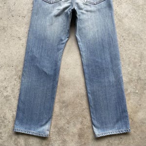 May include: Pale blue denim jeans with a faded appearance. The jeans feature a traditional five-pocket design and a straight leg. The fabric shows signs of wear, enhancing the vintage look. A versatile wardrobe staple.