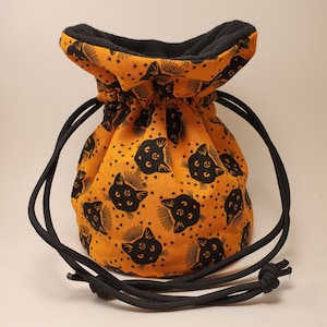 May include: Orange drawstring bag with a black cat print and black drawstring. The bag is lined with black fleece.