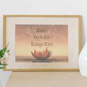 Puede incluir: Una impresión enmarcada con un fondo marrón claro y una flor de loto rosa en el centro. La impresión presenta el texto "Nam Myo Ho Renge Kyo" en una fuente marrón oscura.
