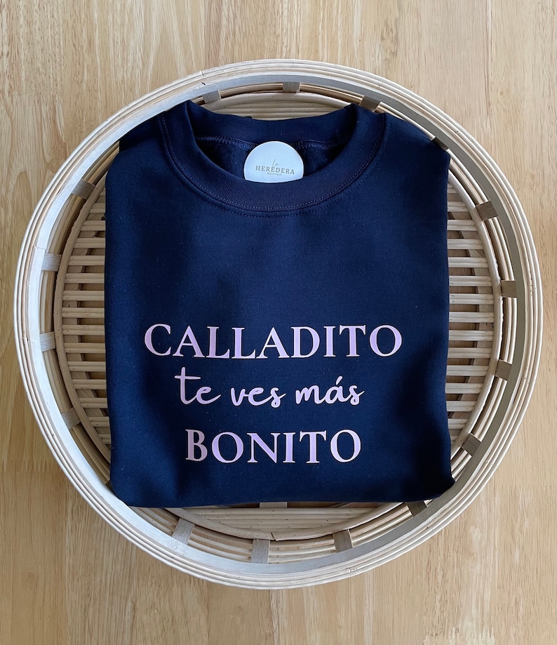 May include: A navy blue sweatshirt with the text "CALLADITO te ves m&aacute;s BONITO" printed in pink.
