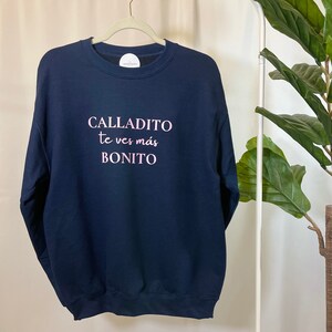 May include: A navy blue sweatshirt with the text "CALLADITO te ves m&aacute;s BONITO" in pink lettering.