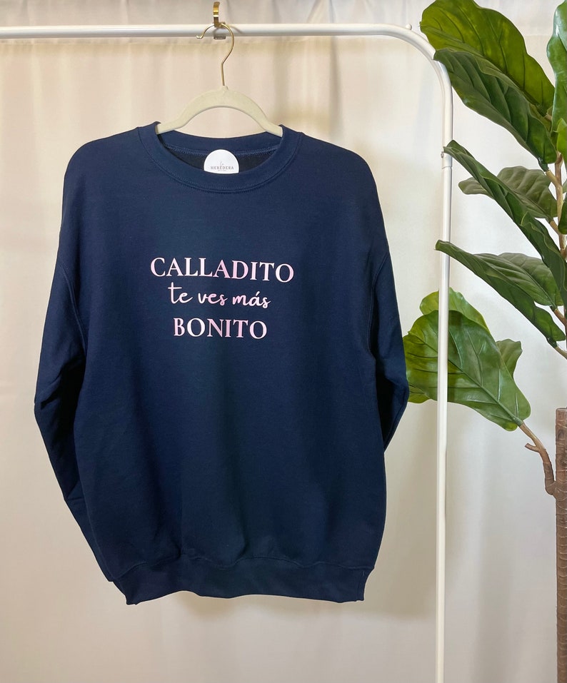 May include: A navy blue sweatshirt with the text "CALLADITO te ves m&aacute;s BONITO" in pink lettering.