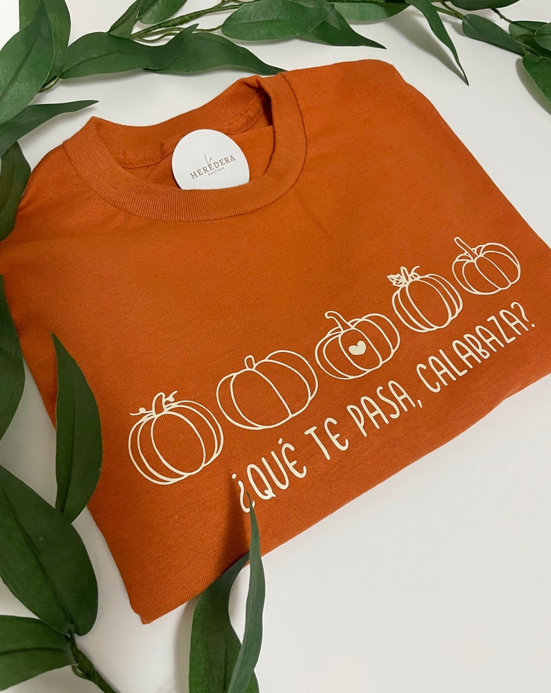 Puede incluir: Una camiseta de color &oacute;xido con un gr&aacute;fico blanco de calabazas y el texto "&iquest;Qu&eacute; te pasa, calabaza?"