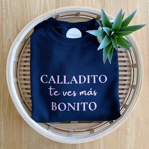 May include: A navy blue sweatshirt with the text "CALLADITO te ves m&aacute;s BONITO" printed in pink.