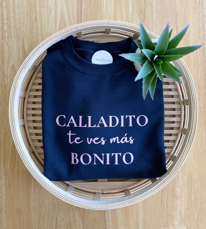 May include: A navy blue sweatshirt with the text "CALLADITO te ves m&aacute;s BONITO" printed in pink.