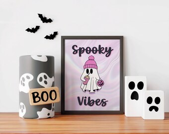 以下が含まれることがあります： 「Spooky Vibes」の文字と、ピンクの帽子をかぶり、飲み物とカボチャを持った漫画の幽霊が描かれた額入りのプリント。白い幽霊のデザインと「BOO」のサインが付いた灰色の円筒、さらに3つの黒いコウモリの装飾。