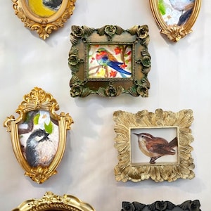 May include: Six ornate gold frames with various bird paintings inside. The frames are all different shapes and sizes, and the birds are depicted in a variety of poses. The frames are arranged in a row on a white wall.