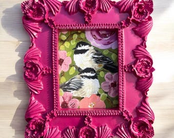 May include: A vibrant fuchsia-colored framed painting. The artwork features two small birds with black and white markings perched among pink flowers and green foliage. The frame has ornate, sculpted details.