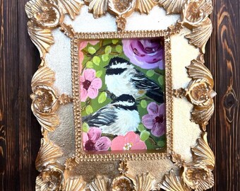 May include: A framed painting of two black-capped chickadees perched on a branch with pink and purple flowers. The frame is gold with ornate details.